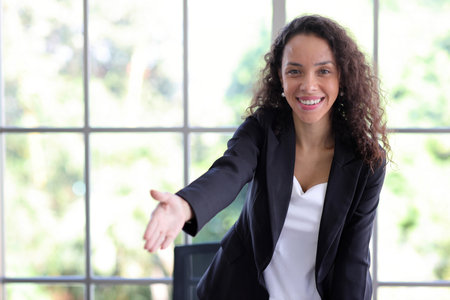 Portrait of confident and beautiful young African businesswoman standing and shaking hand with happy smiling emotion while standing in modern office. Success business conceptの写真素材