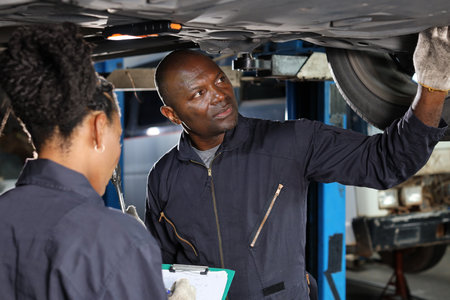 Group of car mechanic in uniform checking maintenance a lifted car service with clipboard at repair garage station. Worker holding wrench and fixing breakdown vehicle. Car repair service conceptの写真素材