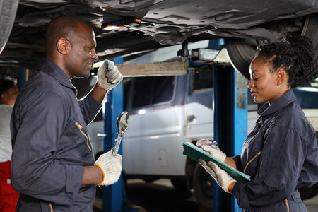 Group of car mechanic in uniform checking maintenance a lifted car service with clipboard at repair garage station. Worker holding wrench and fixing breakdown vehicle. Car repair service conceptの写真素材