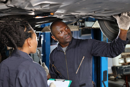 Group of car mechanic in uniform checking maintenance a lifted car service with clipboard at repair garage station. Worker holding wrench and fixing breakdown vehicle. Car repair service conceptの写真素材