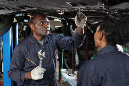 Group of car mechanic in uniform checking maintenance a lifted car service with clipboard at repair garage station. Worker holding wrench and fixing breakdown vehicle. Car repair service conceptの写真素材