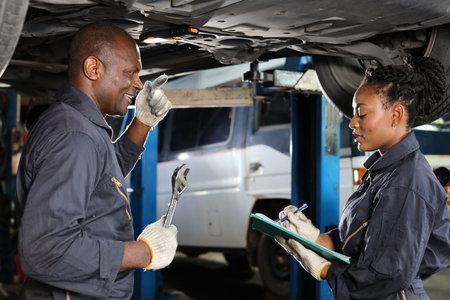 Group of car mechanic in uniform checking maintenance a lifted car service with clipboard at repair garage station. Worker holding wrench and fixing breakdown vehicle. Car repair service conceptの写真素材