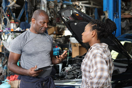 Man technician car mechanical in half uniform show car maintenance service report on tablet at repair garage station. Auto mechanic give customer discussion on her vehicle repair problemsÂ conditionの写真素材
