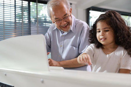 Happy smiling asian senior man sitting and playing piano while teaching grandchild in living room house indorrs. Musical and relaxation makes elder male happiness. Health care lifestyle concept.の写真素材