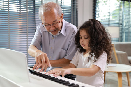 Happy smiling asian senior man sitting and playing piano while teaching grandchild in living room house indorrs. Musical and relaxation makes elder male happiness. Health care lifestyle concept.の写真素材