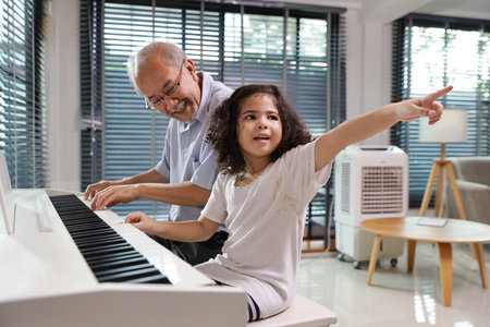 Happy smiling asian senior man sitting and playing piano while teaching grandchild in living room house indorrs. Musical and relaxation makes elder male happiness. Health care lifestyle concept.の写真素材