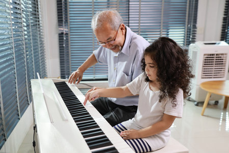 Happy smiling asian senior man sitting and playing piano while teaching grandchild in living room house indorrs. Musical and relaxation makes elder male happiness. Health care lifestyle concept.の写真素材