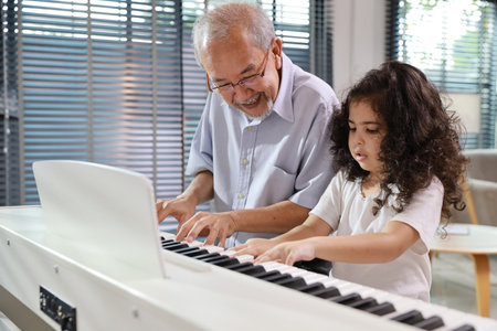 Happy smiling asian senior man sitting and playing piano while teaching grandchild in living room house indorrs. Musical and relaxation makes elder male happiness. Health care lifestyle concept.の写真素材