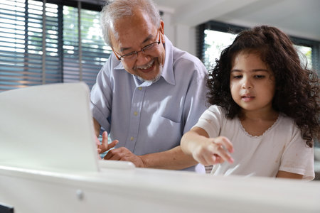 Happy smiling asian senior man sitting and playing piano while teaching grandchild in living room house indorrs. Musical and relaxation makes elder male happiness. Health care lifestyle concept.の写真素材