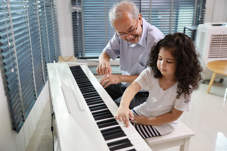 Happy smiling asian senior man sitting and playing piano while teaching grandchild in living room house indorrs. Musical and relaxation makes elder male happiness. Health care lifestyle concept.の写真素材