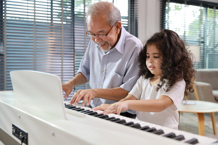 Happy smiling asian senior man sitting and playing piano while teaching grandchild in living room house indorrs. Musical and relaxation makes elder male happiness. Health care lifestyle concept.の写真素材
