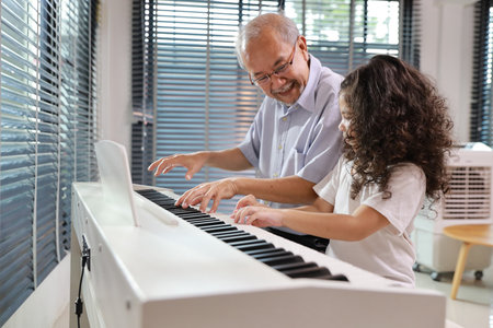 Happy smiling asian senior man sitting and playing piano while teaching grandchild in living room house indorrs. Musical and relaxation makes elder male happiness. Health care lifestyle concept.の写真素材