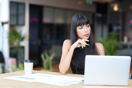 Portrait of confident African businesswoman with happy smiling emotion drinking coffee while sitting and using computer and smart mobile phone on table in restaurant. Success business conceptの写真素材