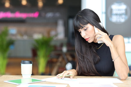 Portrait of confident African businesswoman with happy smiling emotion drinking coffee while sitting and using smart mobile phone and tablet on table in restaurant. Success business conceptの写真素材