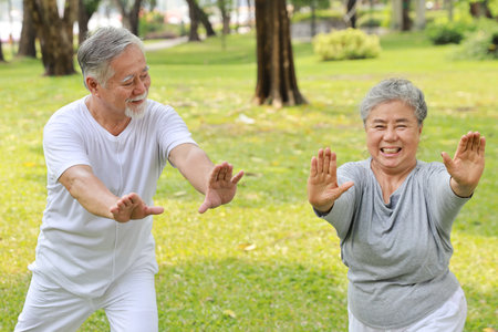 Asian senior couple practice yoga excercise, tai chi tranining, stretching and meditation together with relaxation for healthy in park outdoor after retirement. Happy elderly outdoor lifestyle conceptの写真素材
