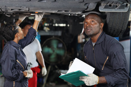 Group of car mechanic in uniform checking maintenance a lifted car service with clipboard at repair garage station. Worker holding wrench and fixing breakdown vehicle. Car repair service conceptの写真素材