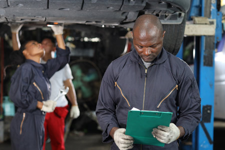 Group of car mechanic in uniform checking maintenance a lifted car service with clipboard at repair garage station. Worker holding wrench and fixing breakdown vehicle. Car repair service conceptの写真素材