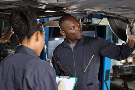 Group of car mechanic in uniform checking maintenance a lifted car service with clipboard at repair garage station. Worker holding wrench and fixing breakdown vehicle. Car repair service conceptの写真素材