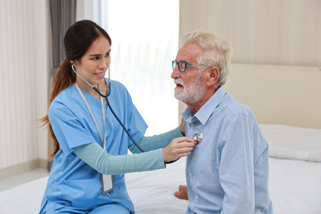Happy caregiver examining senior elderly man patient listening heartbeat using stethoscopeÂ on bed at retirement house. Asian smiling nurse taking good help care and support of elder patient at house.の写真素材
