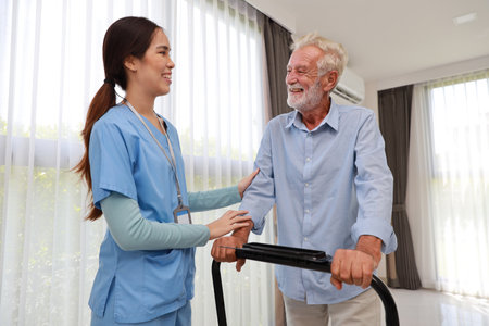Happy caregiver helping senior elderly man walk with exercise machine in bedroom at home or retirement house. Asian smiling nurse taking good help care and support of elder patient at house.の写真素材