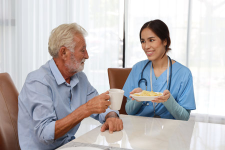 Happy caregiver try stopping senior caucasian man eating potato chips or junk food and taking medicine after breakfast in living room at retirement house. Unhealthy and junk food lifestyle conceptの写真素材