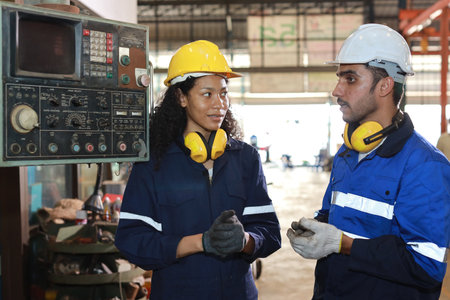 Technician engineer woman in protective uniform with hardhat standing and teaching apprentices or colleague worker to use computerized machine control at heavy industry manufacturing factoryの写真素材