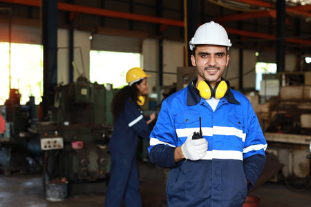 Technician engineer man in protective suit stand and use walkie talkie radio and tablet while controll or maintenance operation work lathe metal machine at heavy industry manufacturing factoryの写真素材