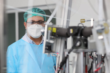 Worker in personal protective equipment or PPE inspecting quality of mask and medical face mask production line in factory, manufacturing industry and factory concept.の写真素材