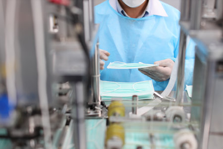 Inspector or worker hands with nitrile gloves doing quality of mask and medical face mask production line, Industry and factory concept.の写真素材