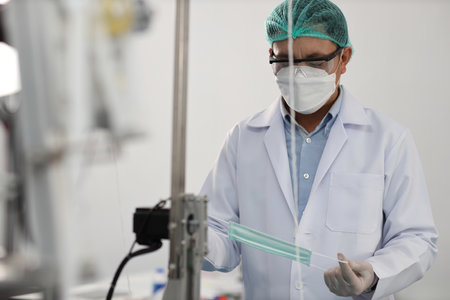 Worker in personal protective equipment or PPE inspecting quality of mask and medical face mask production line in factory, manufacturing industry and facの写真素材