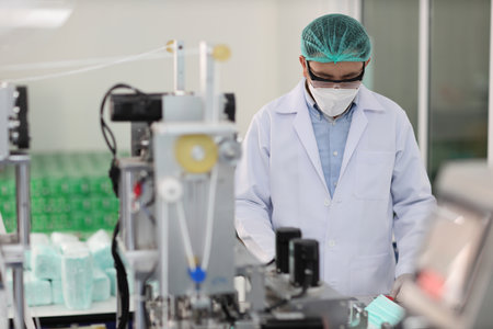 Worker in personal protective equipment or PPE inspecting quality of mask and medical face mask production line in factory, manufacturing industry and factory concept.の写真素材