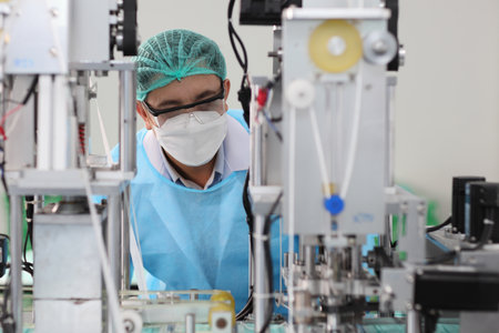 Worker in personal protective equipment or PPE inspecting quality of mask and medical face mask production line in factory, manufacturing industry and factory concept.の写真素材