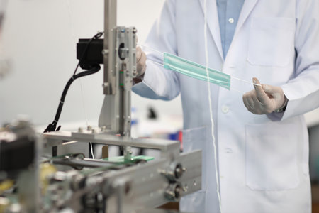 Worker hands in personal protective equipment or PPE inspecting quality of mask and medical face mask production line in factory, manufacturing industry and factory concept.の写真素材