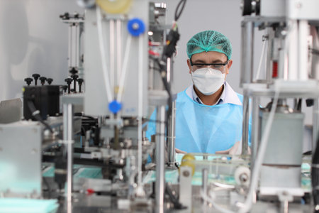 Worker in personal protective equipment or PPE inspecting quality of mask and medical face mask production line in factory, manufacturing industry and factory concept.の写真素材