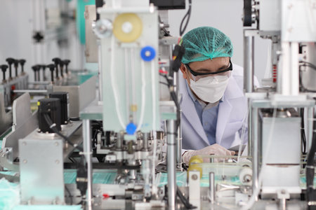 Worker in personal protective equipment or PPE inspecting quality of mask and medical face mask production line in factory, manufacturing industry and factory concept.の写真素材