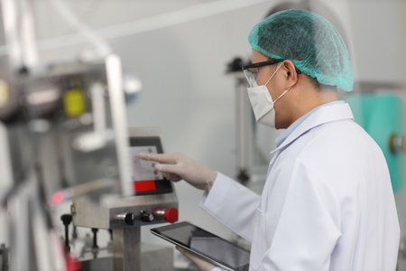Worker man in personal protective equipment or PPE inspecting quality of mask and medical face mask production line in factory, manufacturing industry and factory concept.の写真素材