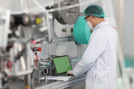 Inspector man or worker male doing quality of mask and medical face mask production line with blank green screen computer, Industry and factory concept.の写真素材