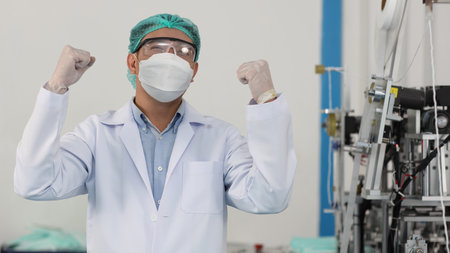 Worker in personal protective equipment or PPE inspection quality raising hands with exciting emotion in mask and medical face mask production line factory, manufacturing industry and factory concept.の写真素材