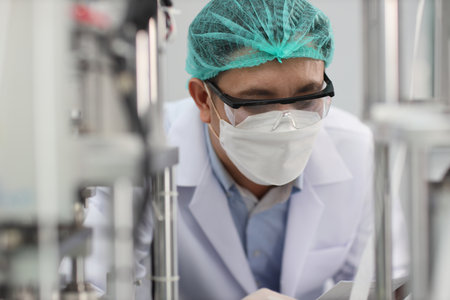 Worker in personal protective equipment or PPE inspecting quality of mask and medical face mask production line in factory, manufacturing industry and factory concept.の写真素材