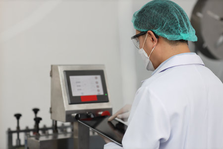 Worker in personal protective equipment or PPE inspecting quality of mask and medical face mask production line in factory, manufacturing industry and factory concept.の写真素材