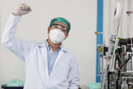 Worker in personal protective equipment or PPE inspection quality raising hands with exciting emotion in mask and medical face mask production line factory, manufacturing industry and factory concept.の写真素材