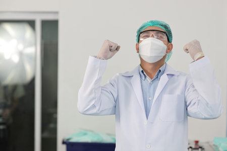 Worker in personal protective equipment or PPE inspection quality raising hands with exciting emotion in mask and medical face mask production line factory, manufacturing industry and factory concept.の写真素材