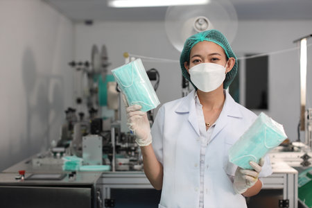 Worker woman in personal protective equipment or PPE inspecting quality of mask and medical face mask production line in factory, manufacturing industry and factory concept.の写真素材