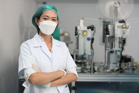 Worker in personal protective equipment or PPE inspection quality crossed arms and looking camera in mask and medical face mask production line factory, manufacturing industry and factory concept.の写真素材