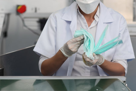 Worker woman hands in personal protective equipment or PPE inspecting quality of mask and medical face mask production line in factory, manufacturing industry and factory concept.の写真素材
