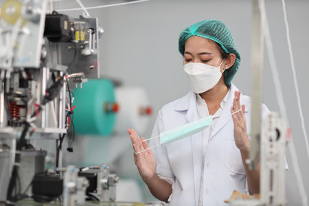 Worker woman in personal protective equipment or PPE inspecting quality of mask and medical face mask production line in factory, manufacturing industry and factory concept.の写真素材