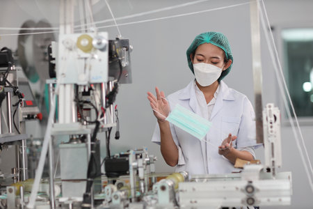 Worker woman in personal protective equipment or PPE inspecting quality of mask and medical face mask production line in factory, manufacturing industry and factory concept.の写真素材