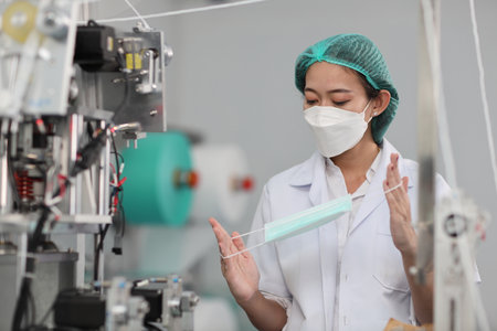 Worker woman in personal protective equipment or PPE inspecting quality of mask and medical face mask production line in factory, manufacturing industry and factory concept.の写真素材
