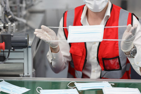 Caucasian mechanic technician maintenance hands or PPE inspecting quality of mask and medical face mask production line in factory, manufacturing industry and factory concept.の写真素材