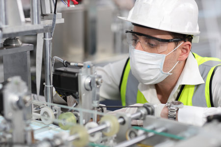 Caucasian mechanic technician maintenance, repairing industrial machinery equipment in factory. Professional worker in protective clothing with goggles and mask using wrench at manufacturing factoryの写真素材